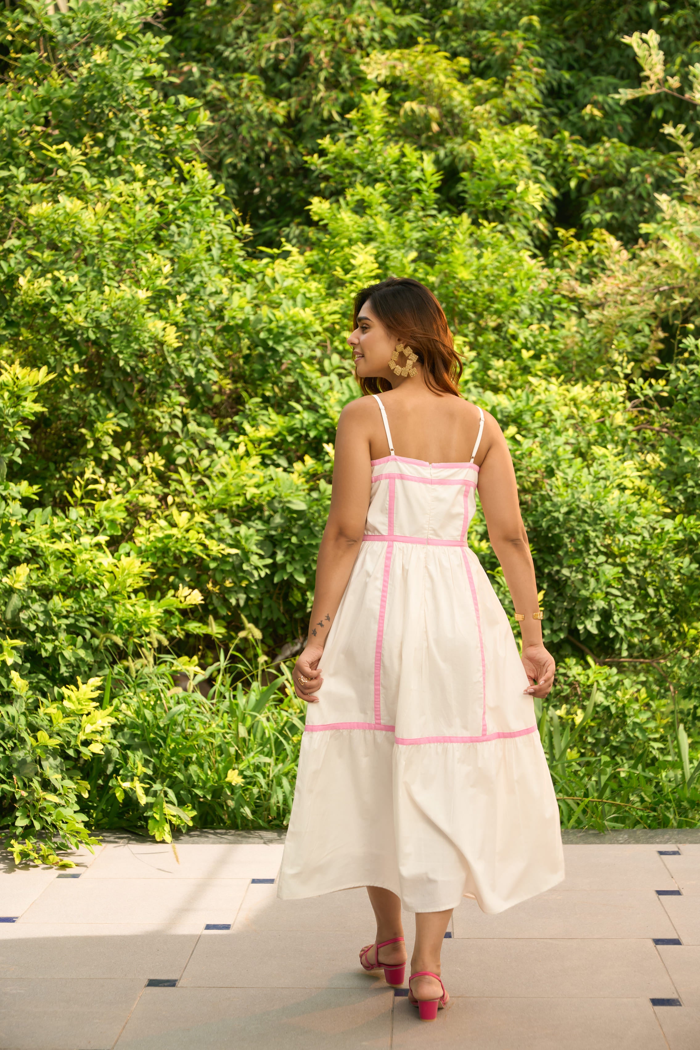 Woman wearing an Amalfi dress with pink trim walking outdoors surrounded by greenery
