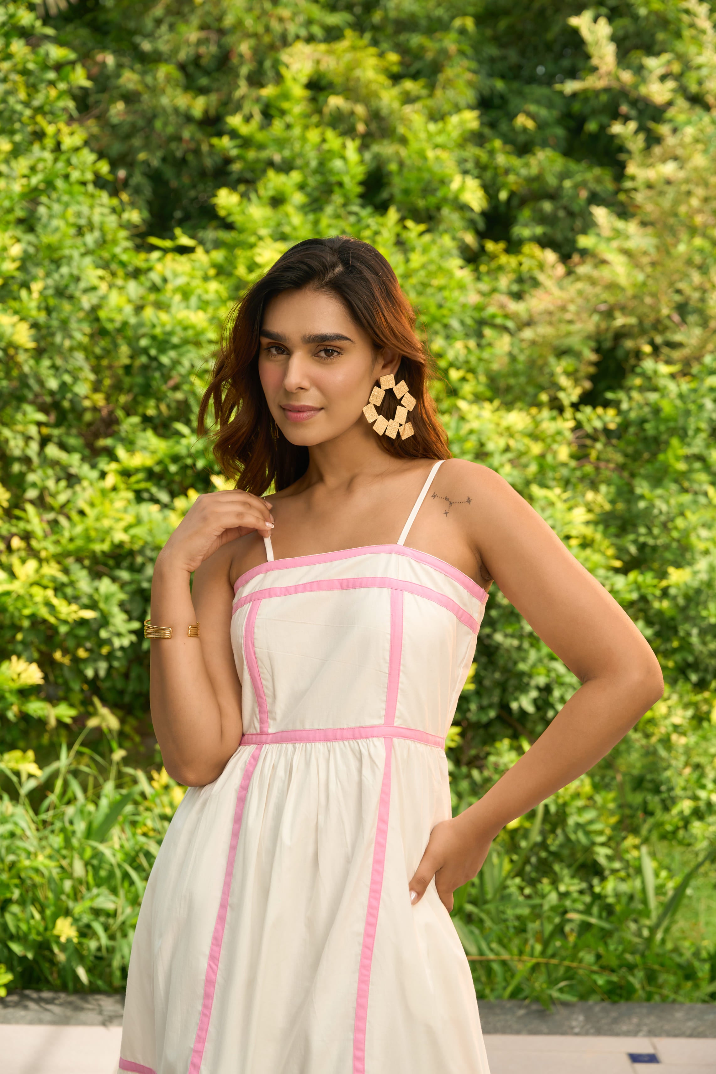 Woman wearing an Amalfi dress with pink trim featuring spaghetti straps and a flowy skirt in outdoor garden setting