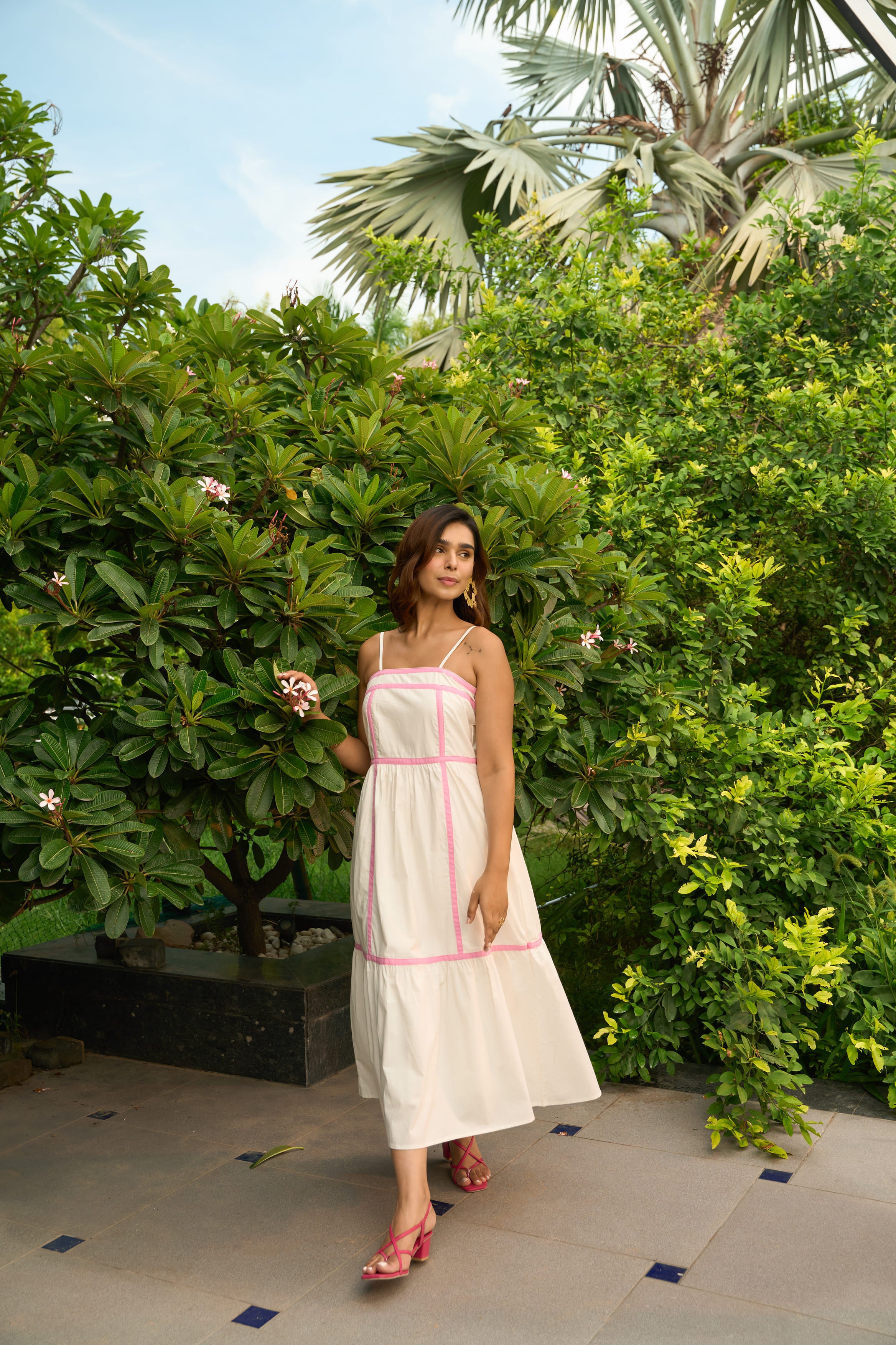 Woman wearing an Amalfi dress with pink trim standing outdoors near lush green plants