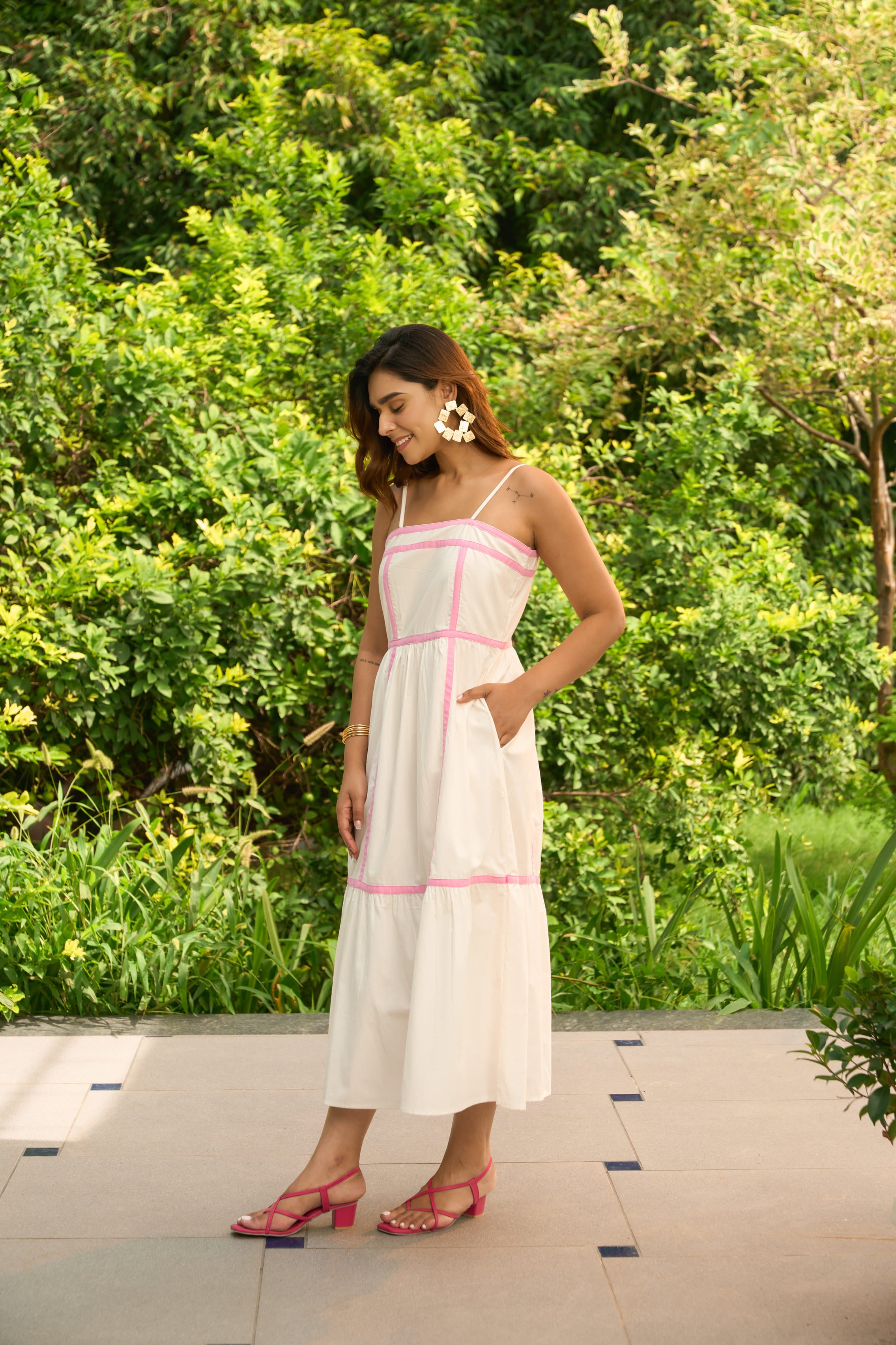 Woman wearing an Amalfi dress with pink trim standing outdoors with green foliage background