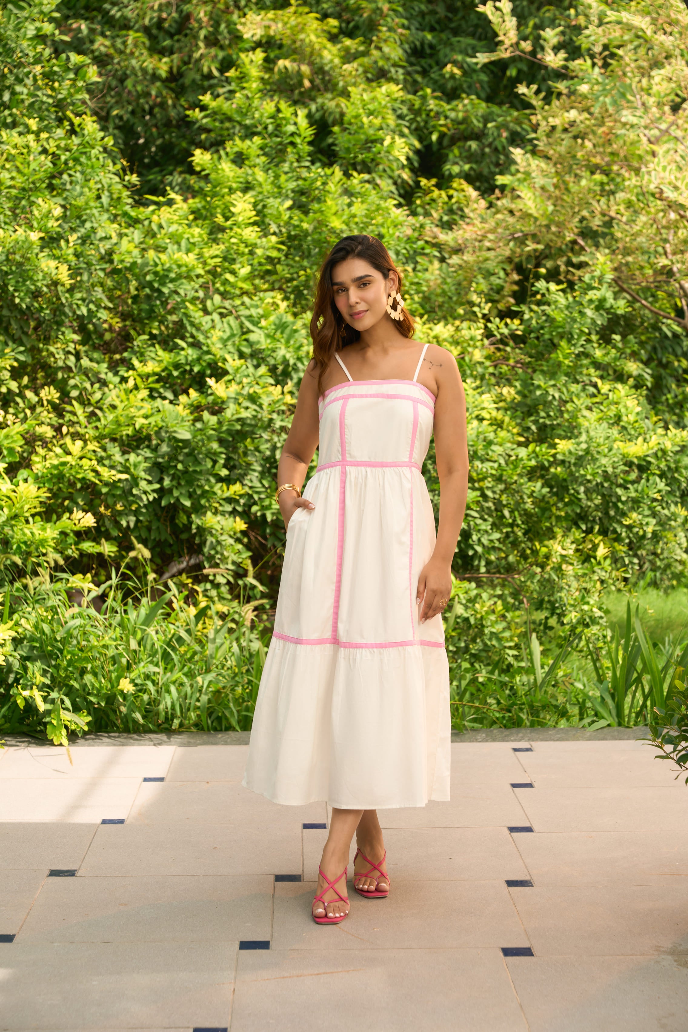 Woman wearing Amalfi dress with pink trim standing outdoors on patio surrounded by greenery