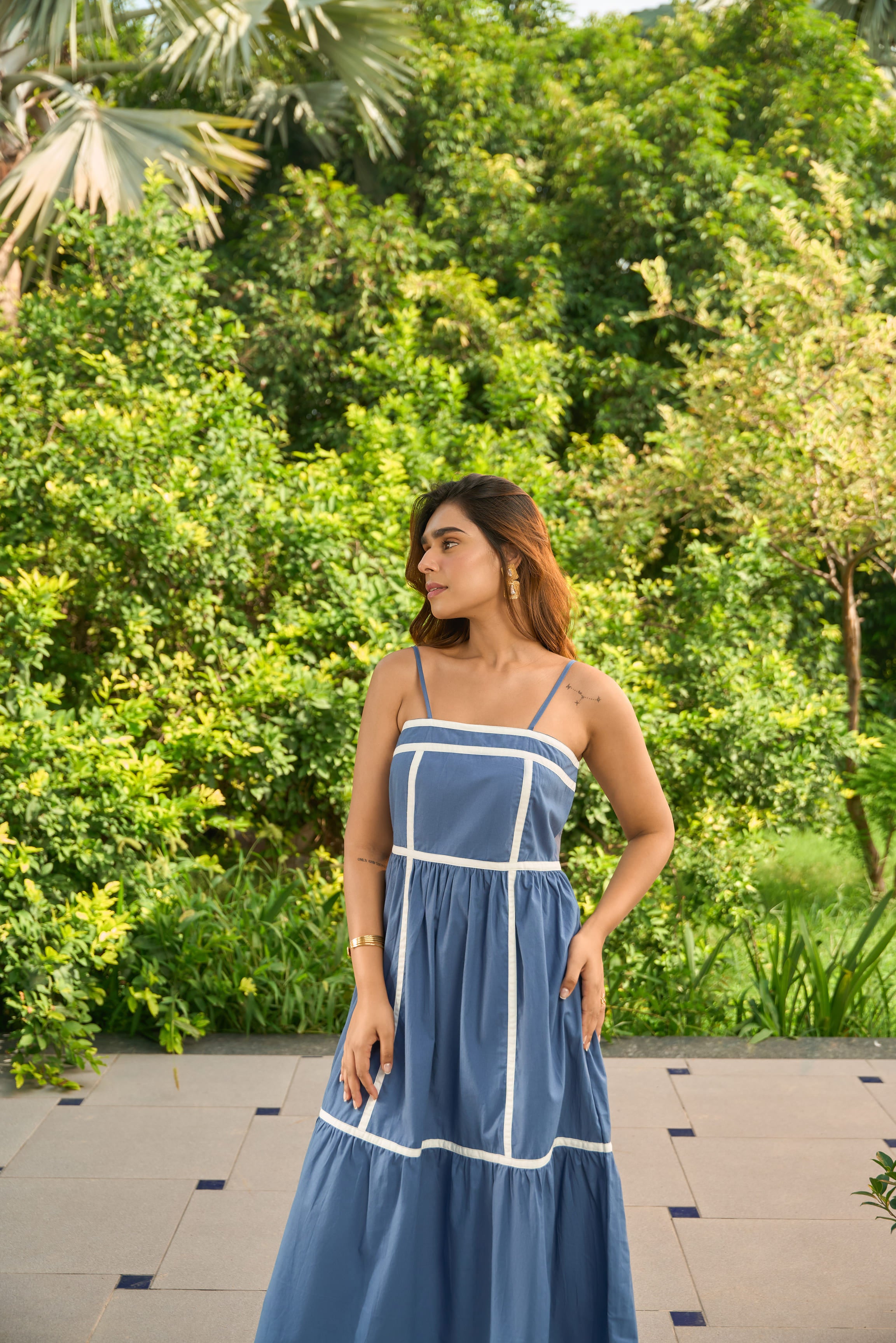 Woman wearing a Santorini blue sundress with white trim standing outdoors in a garden