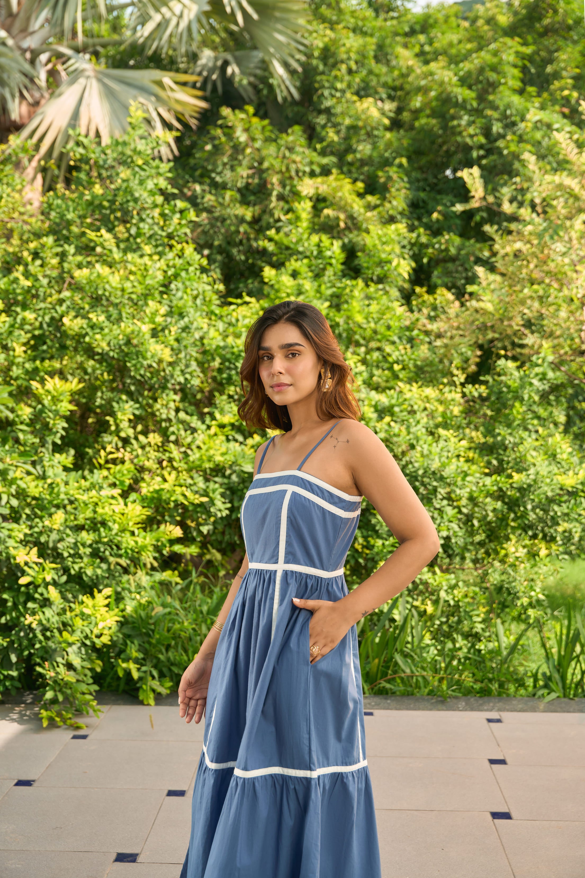 Woman wearing Santorini blue sundress with white trim outdoors near green foliage